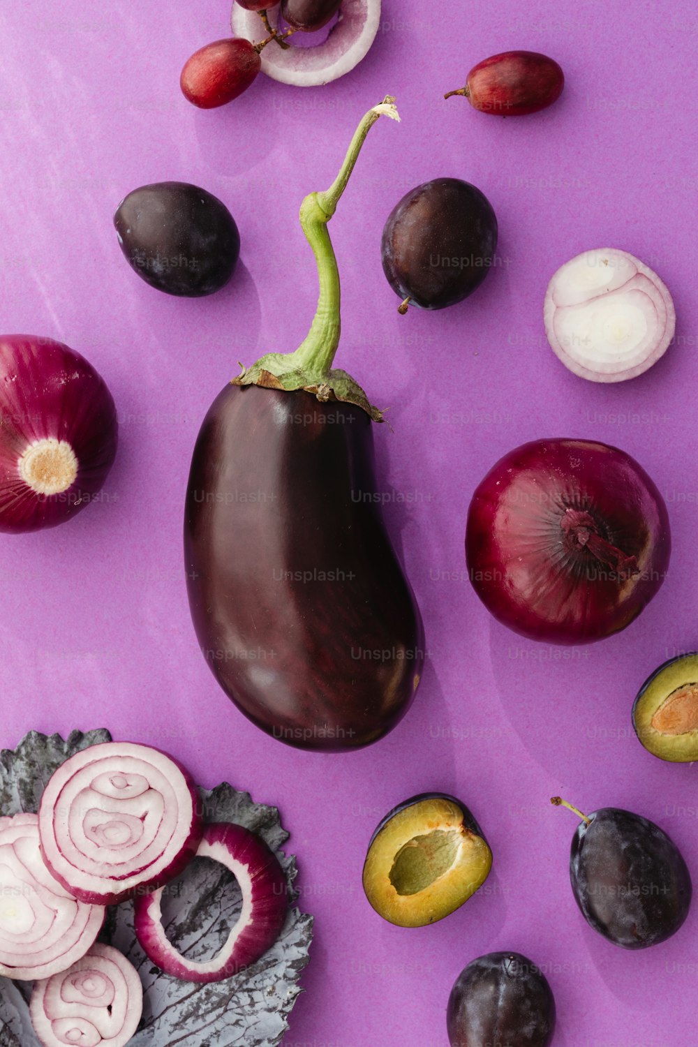 una berenjena, cebolla, rodajas de cebolla y otras verduras en un púrpura