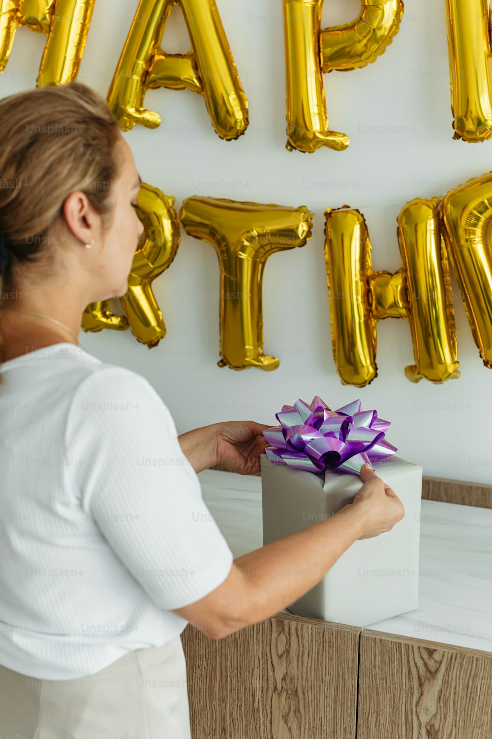 a woman holding a gift box in front of a happy birthday sign