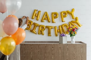 a woman holding a bunch of balloons in front of a happy birthday sign