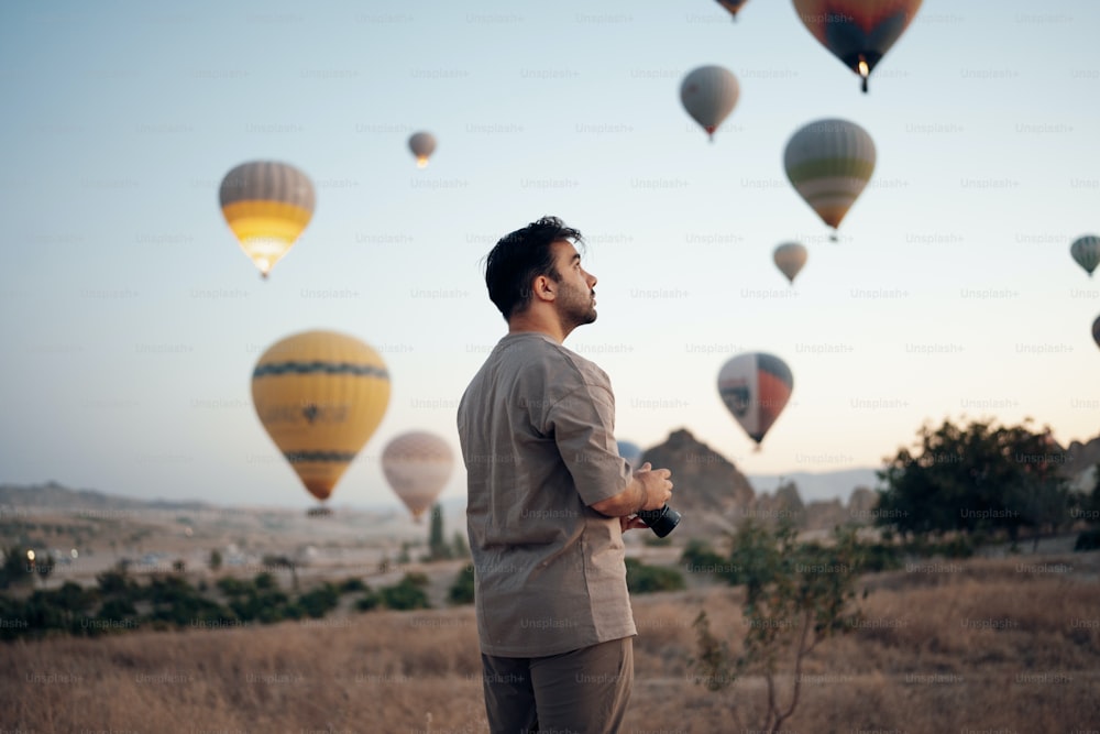 a man standing in a field surrounded by hot air balloons