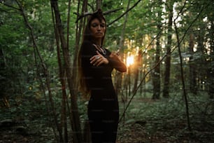 a woman standing in the woods with her arms crossed
