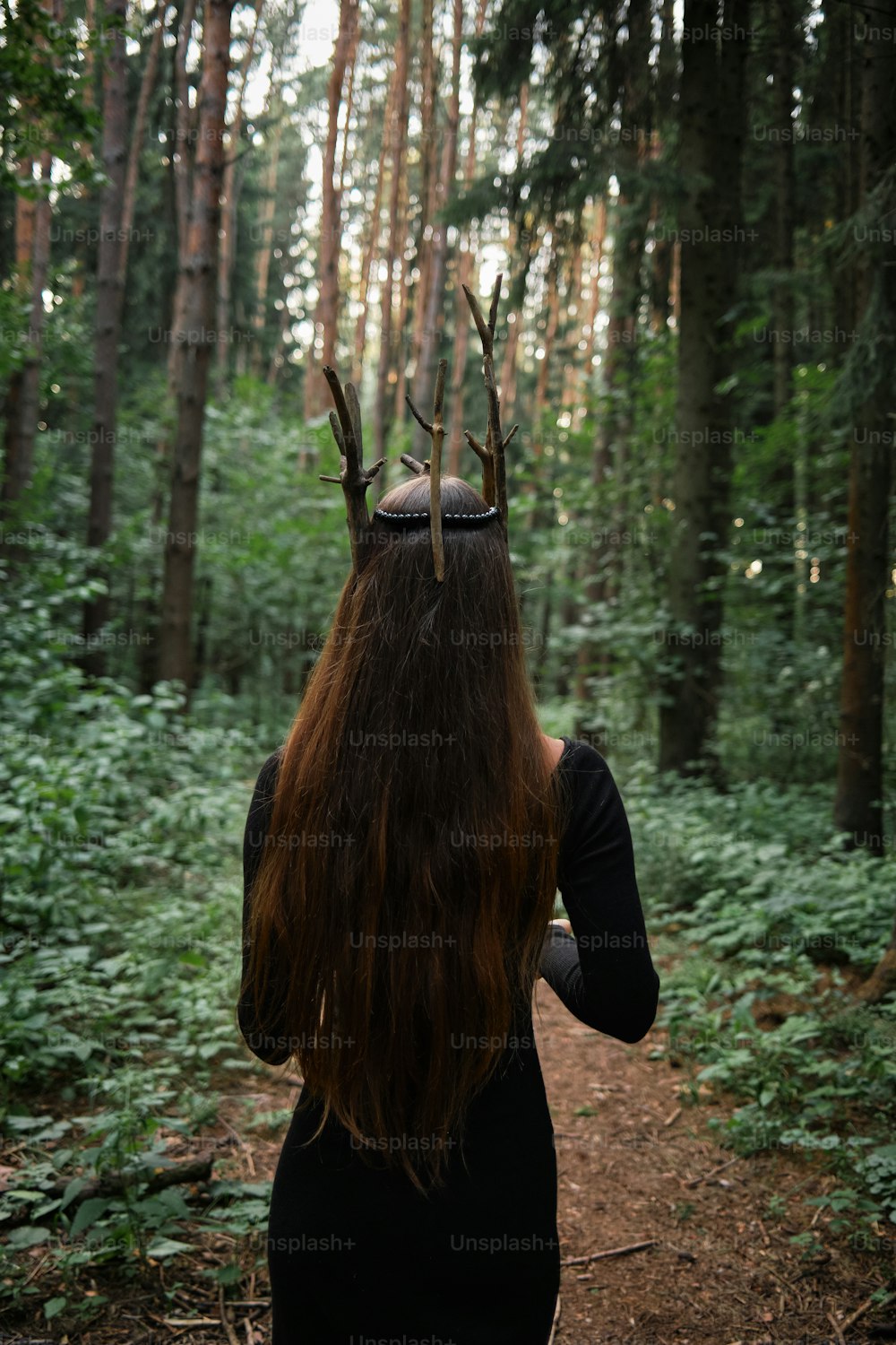 a woman with a deer's antlers on her head walking through a forest