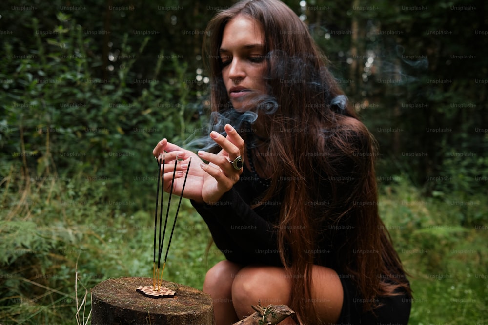 a woman sitting on a stump smoking a cigarette