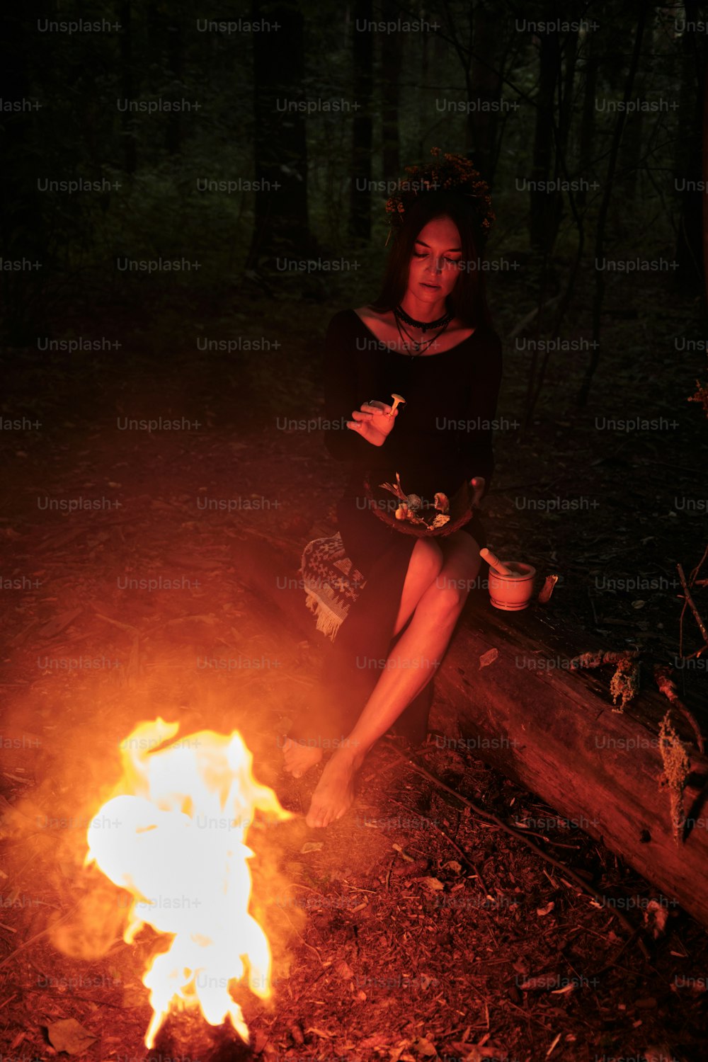 uma mulher sentada em um tronco ao lado de um incêndio