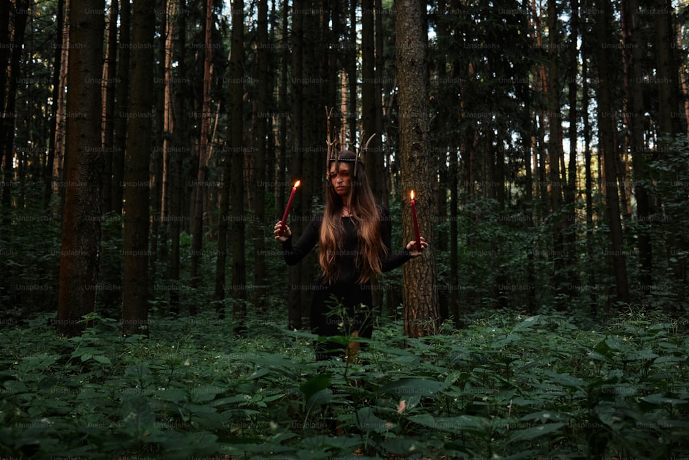 a woman holding two candles in a forest