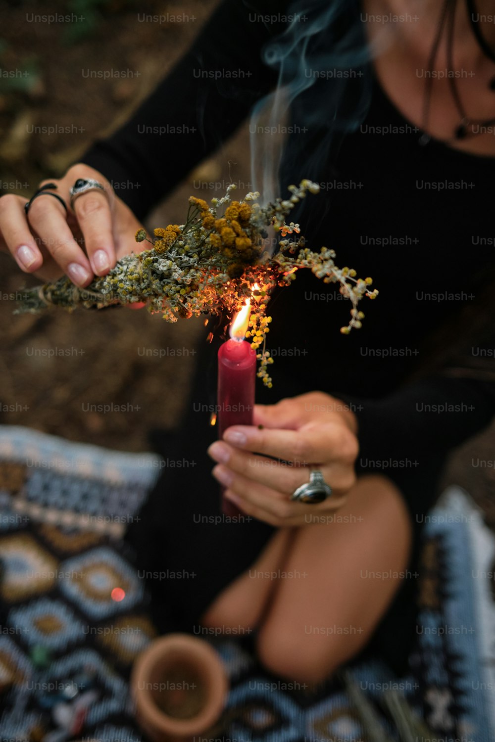 Una mujer sentada sobre una manta sosteniendo una vela encendida