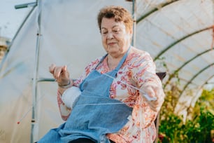 an older woman is knitting in a greenhouse