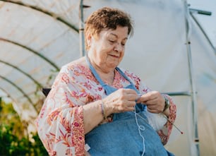 an older woman knitting in a greenhouse