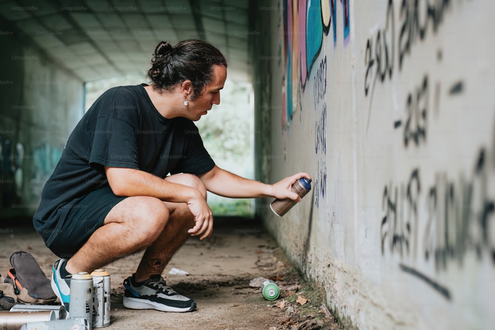 a man kneeling down next to a wall with graffiti on it