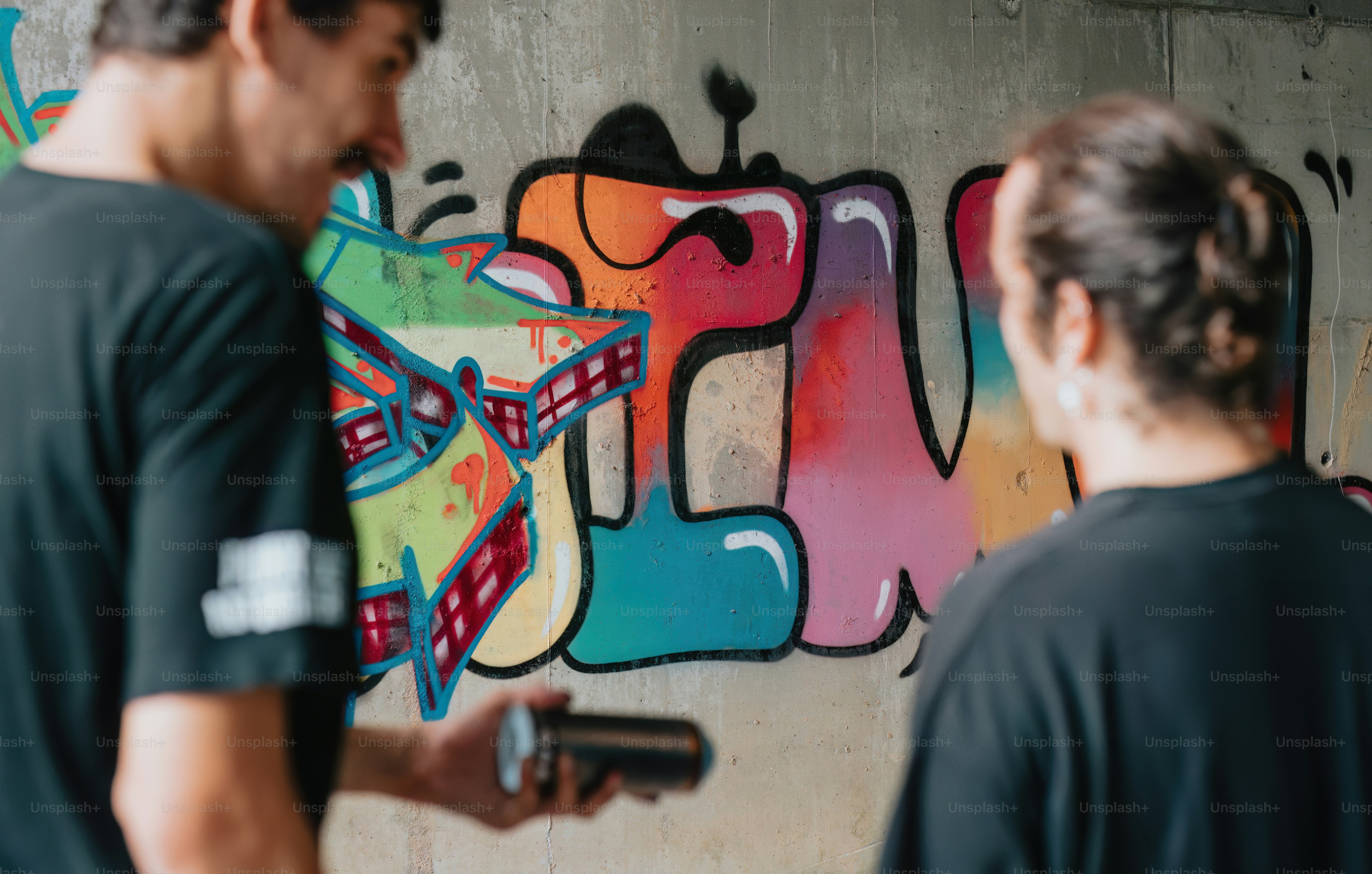 a couple of men standing in front of a graffiti covered wall