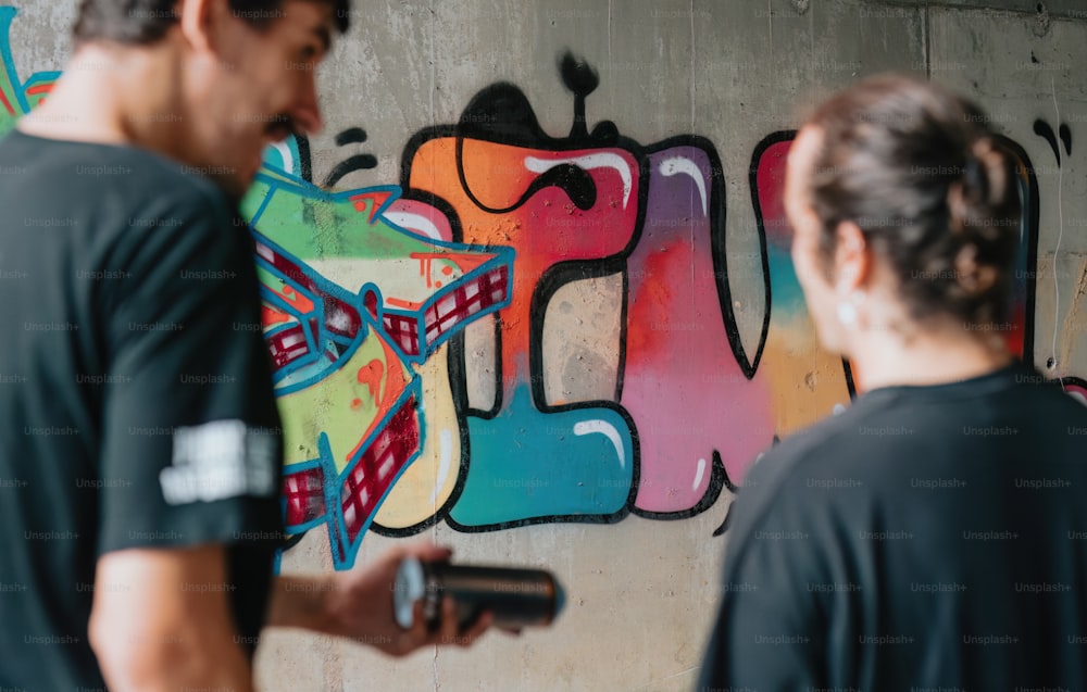 Un par de hombres parados frente a una pared cubierta de graffiti