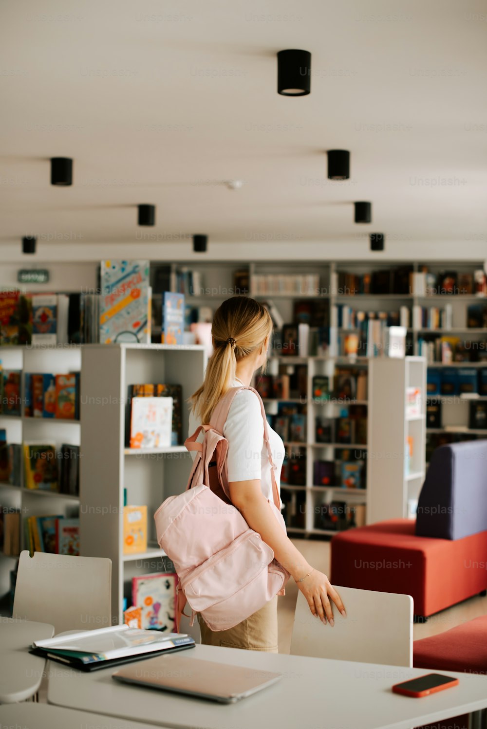 uma mulher com uma mochila rosa em pé em uma biblioteca