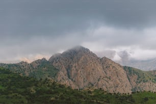 una cadena montañosa con árboles y nubes al fondo