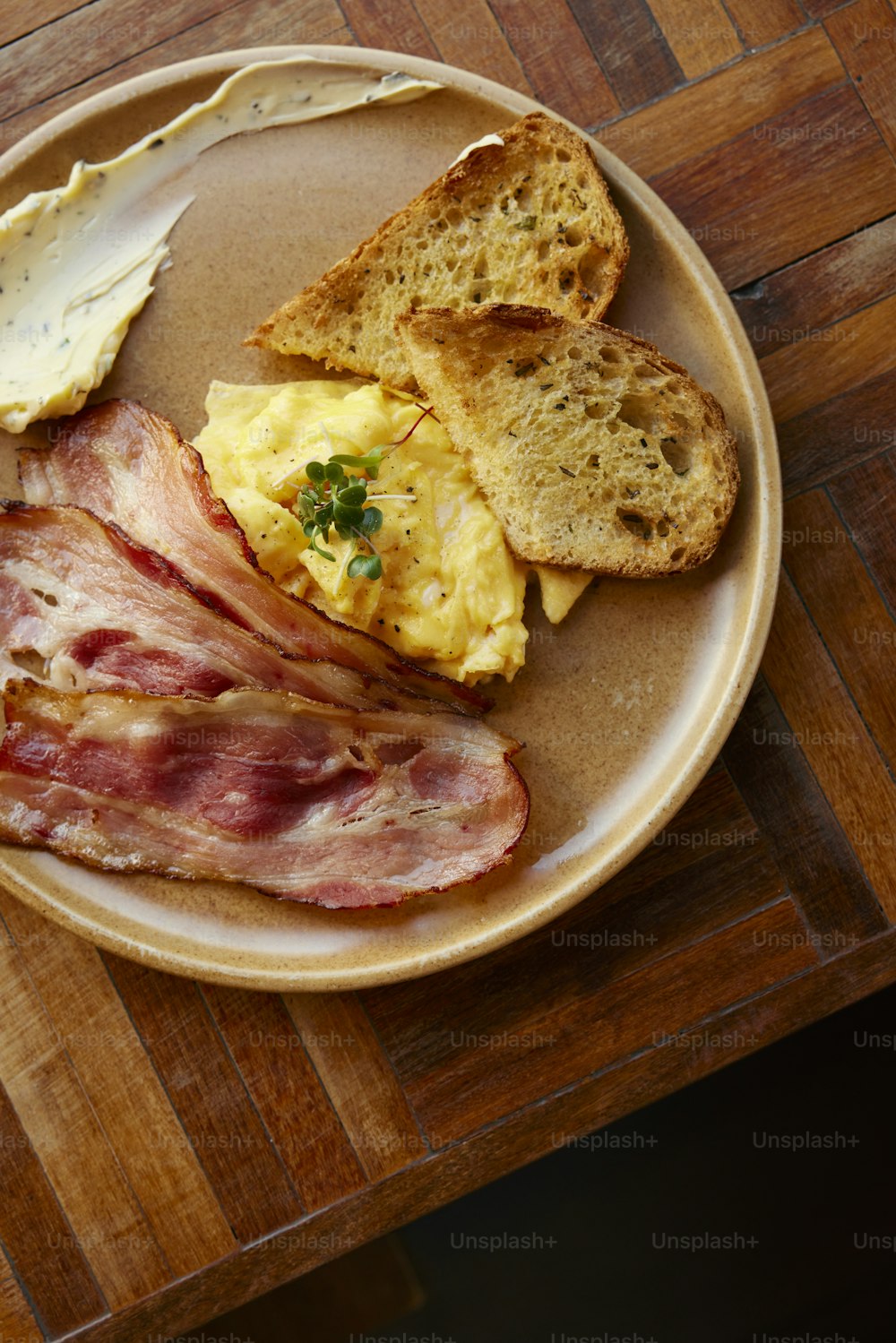 a plate of bacon, bread, and eggs on a wooden table