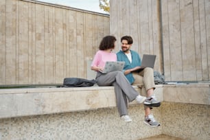 a man and a woman sitting on a ledge with a laptop