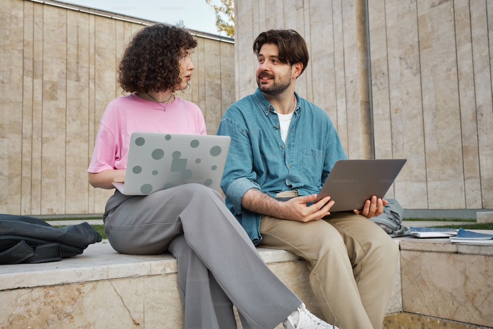a man and a woman sitting on a bench with laptops