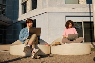 a man and a woman sitting on a couch using laptops