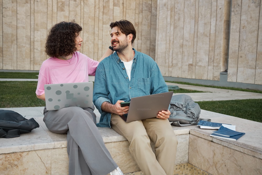 a man and a woman sitting on a wall with laptops