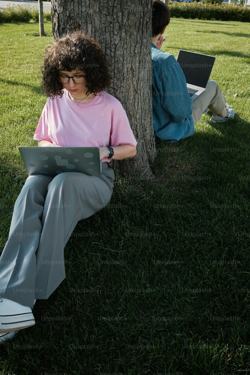 a woman sitting under a tree using a laptop computer