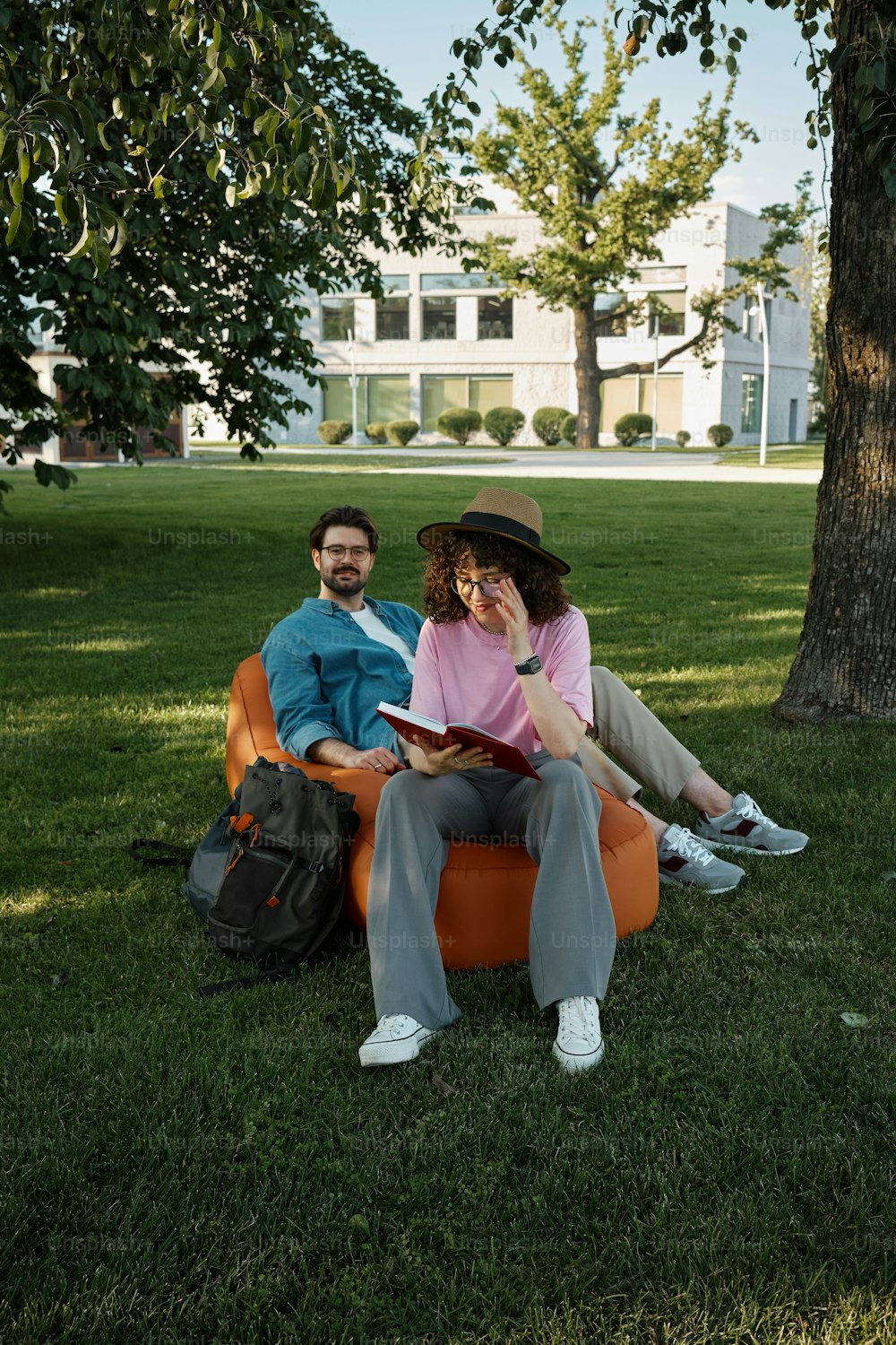 a man and woman sitting on an orange chair under a tree