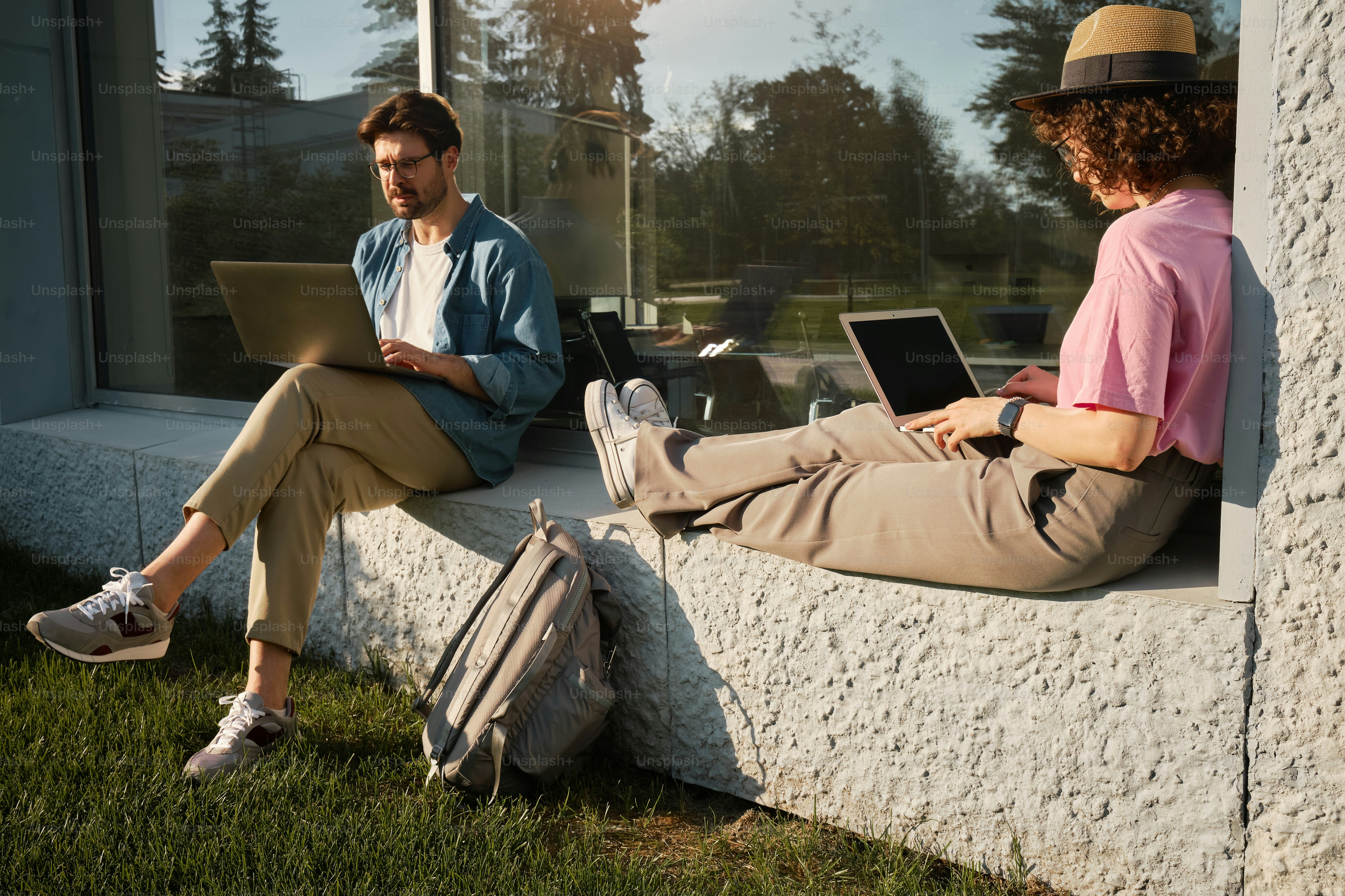 Ein Mann und eine Frau, die mit Laptops an einer Wand sitzen