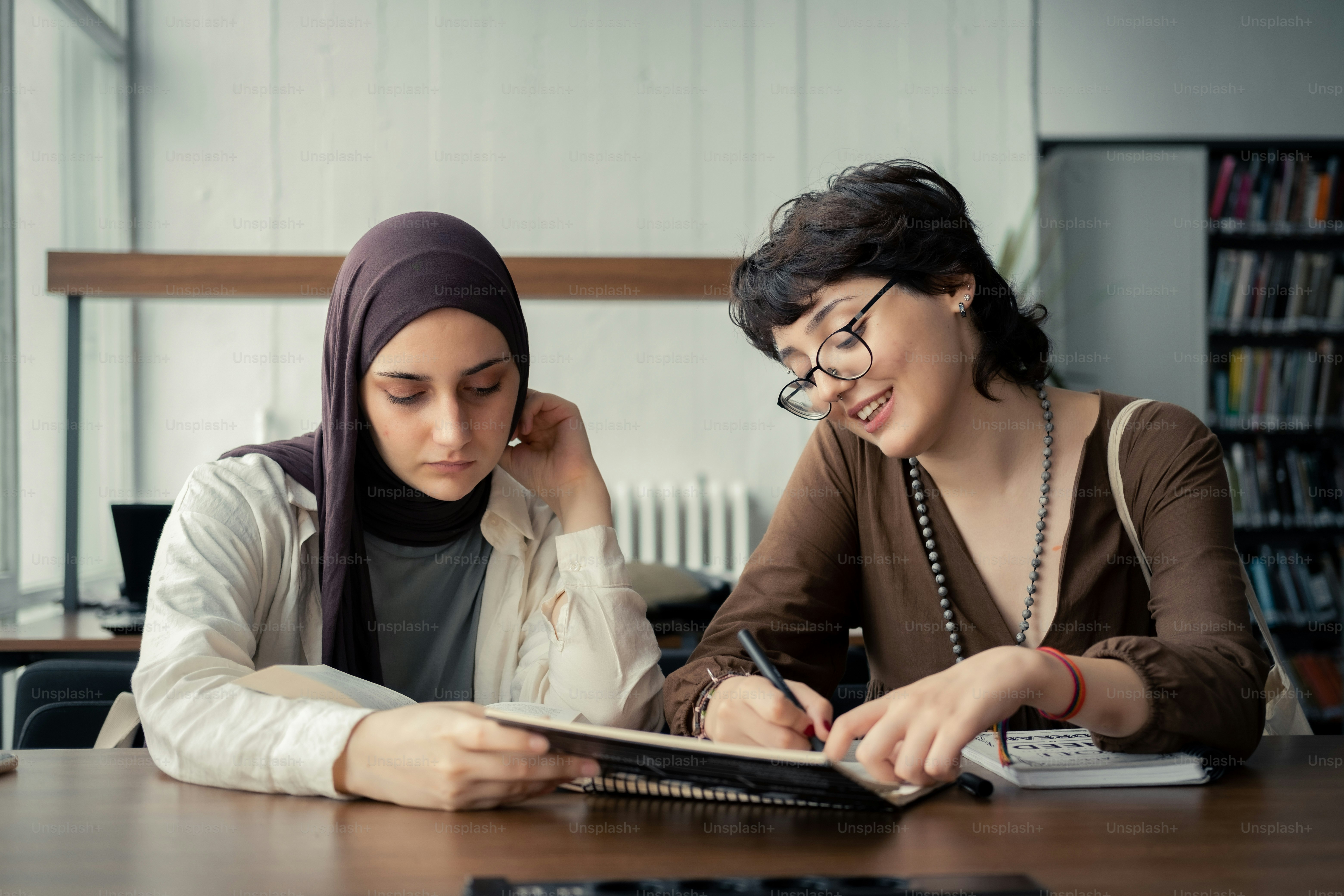 two women sitting at a table with a book