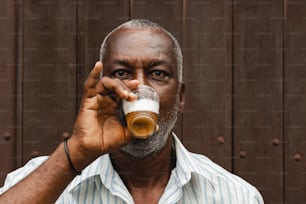 a man drinking a glass of beer in front of a wooden wall