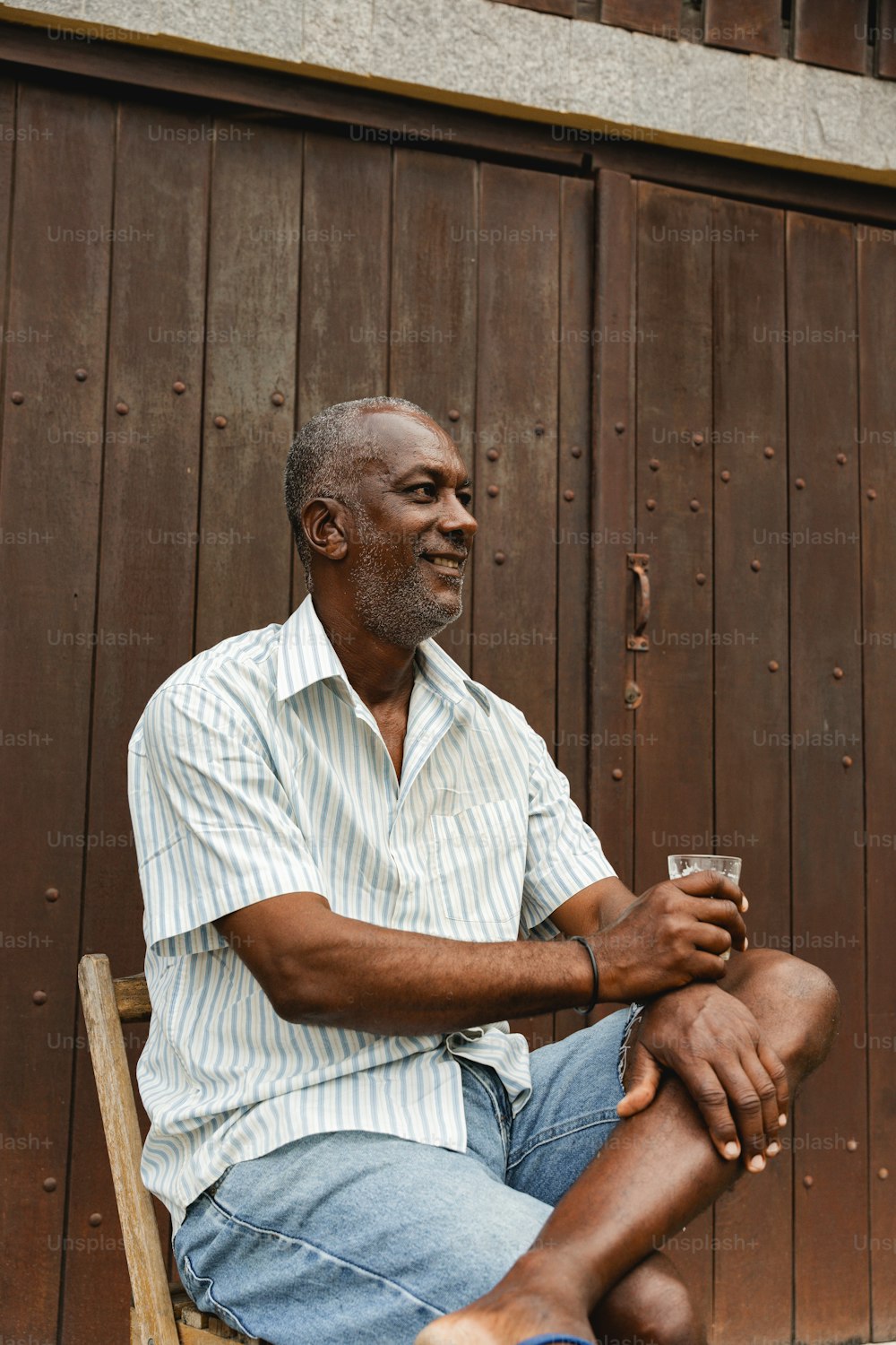 한 남자가 나무 의자에 앉아 와인 한 잔을 들고 있다