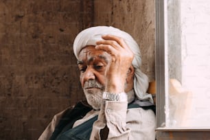 a man with a white turban leaning against a wall