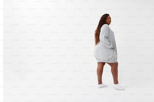 eine Frau in einem grauen Pulloverkleid und weißen Tennisschuhen