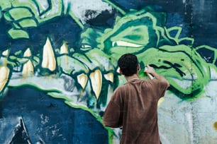 a man painting a wall with green and blue graffiti