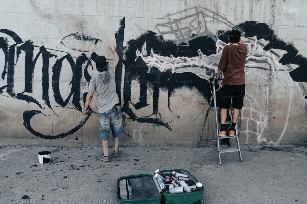 a couple of men painting a wall with graffiti