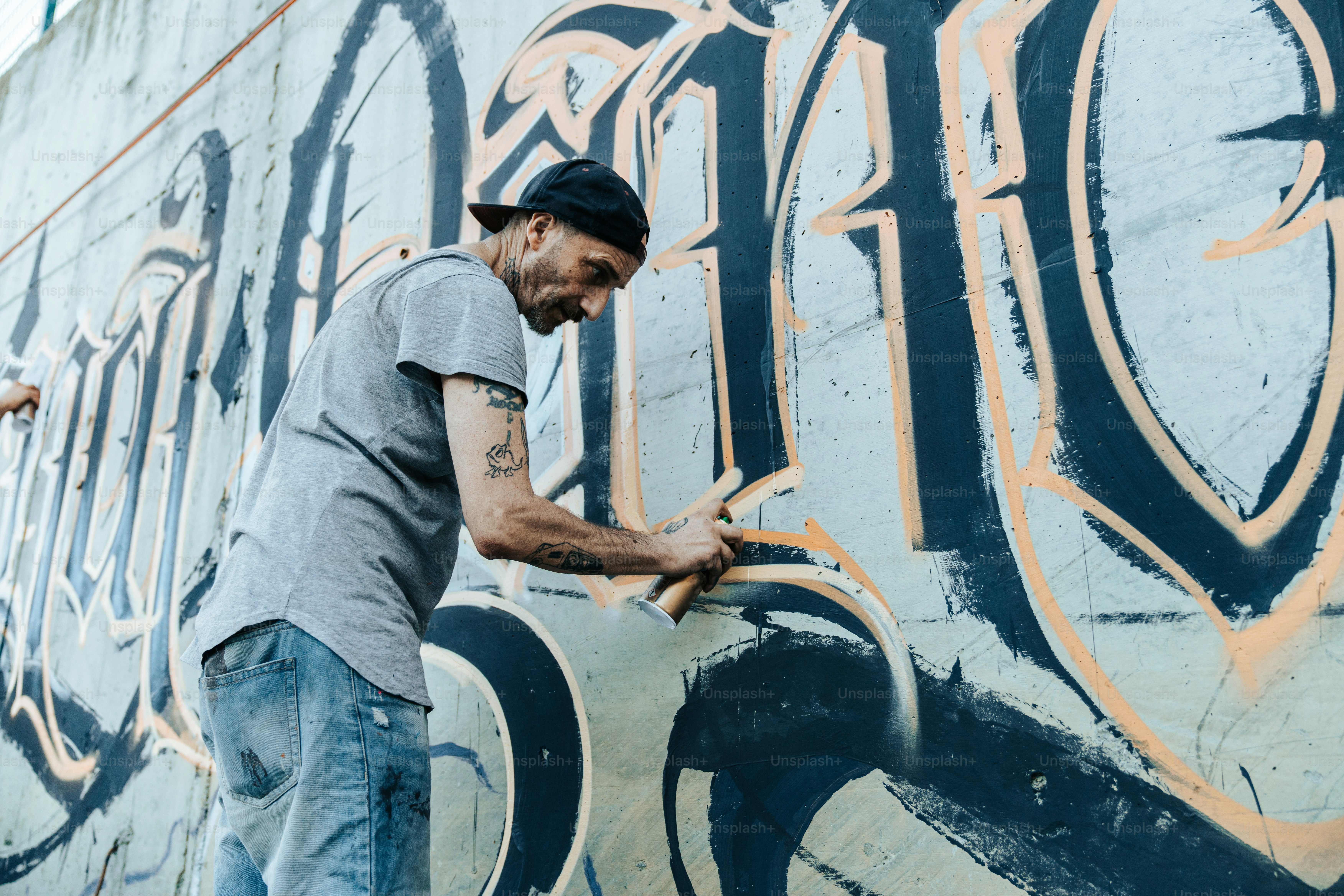Un hombre pintando una pared con graffiti foto – Imagen de Arte ...