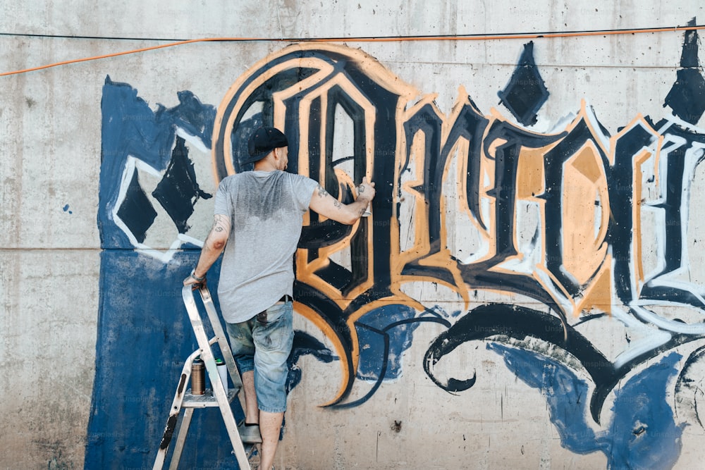 Ein Mann auf einer Leiter malt Graffiti an eine Wand