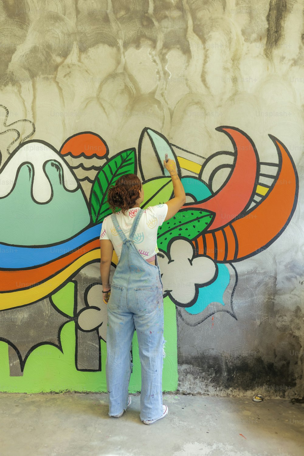 a woman in overalls painting a mural on a wall