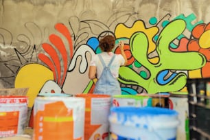 a woman in overalls painting a wall with graffiti