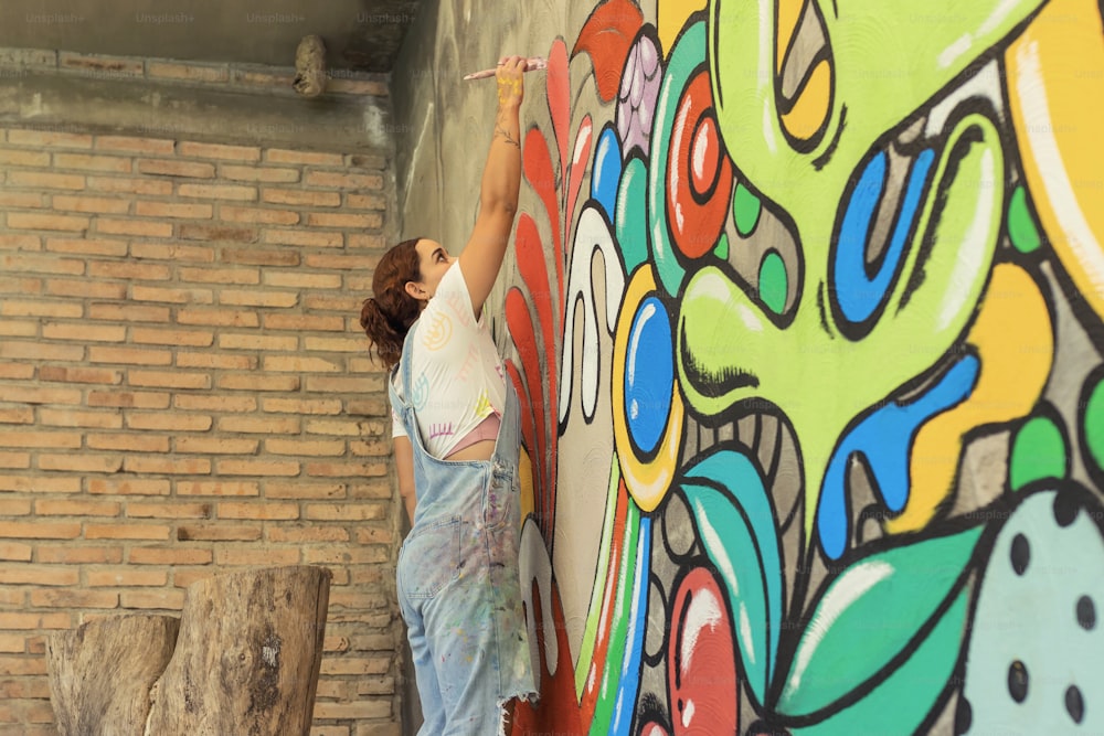 a woman painting a mural on a brick wall