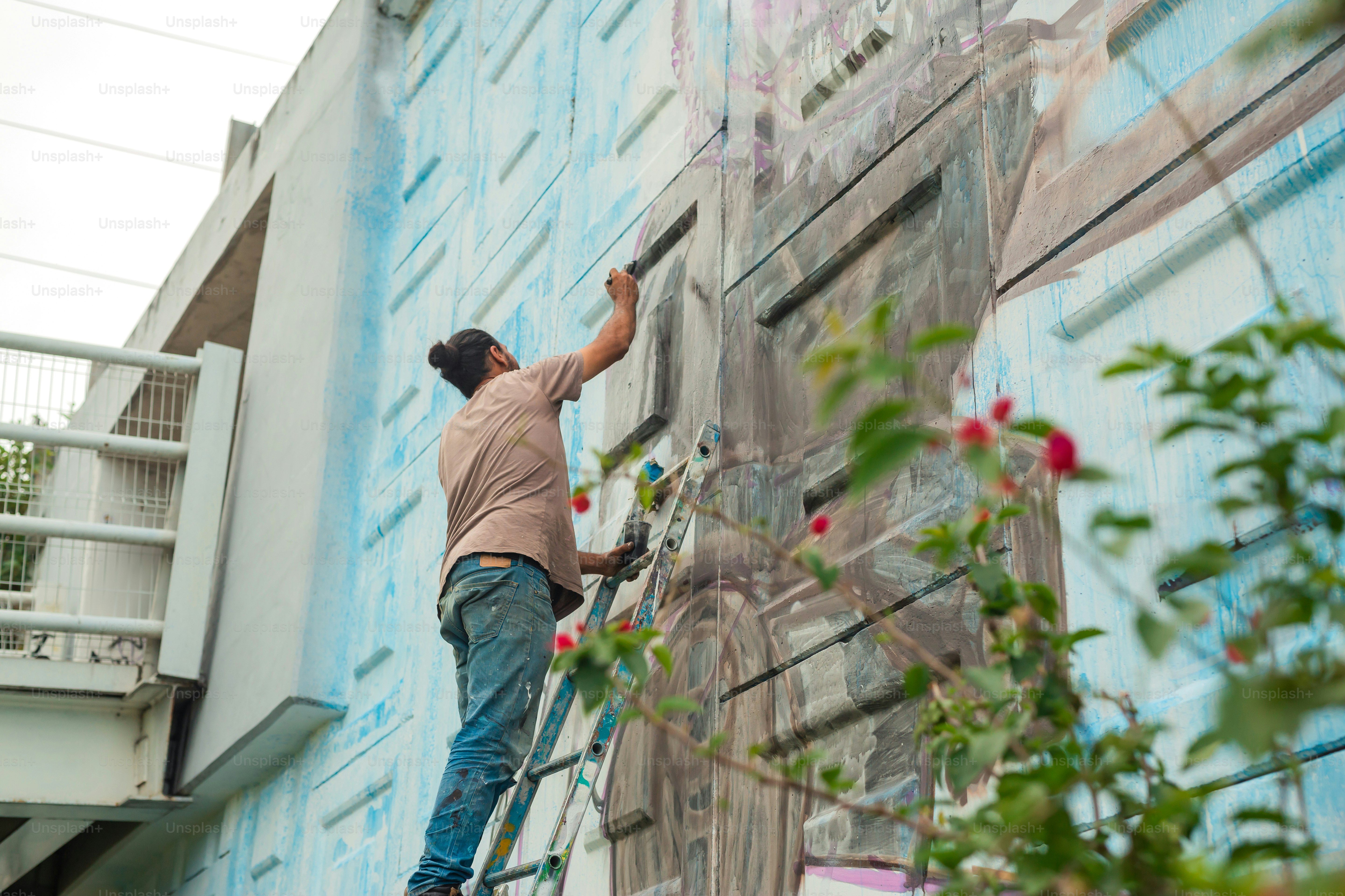 A man is painting a mural on the side of a building photo – Mural Image ...