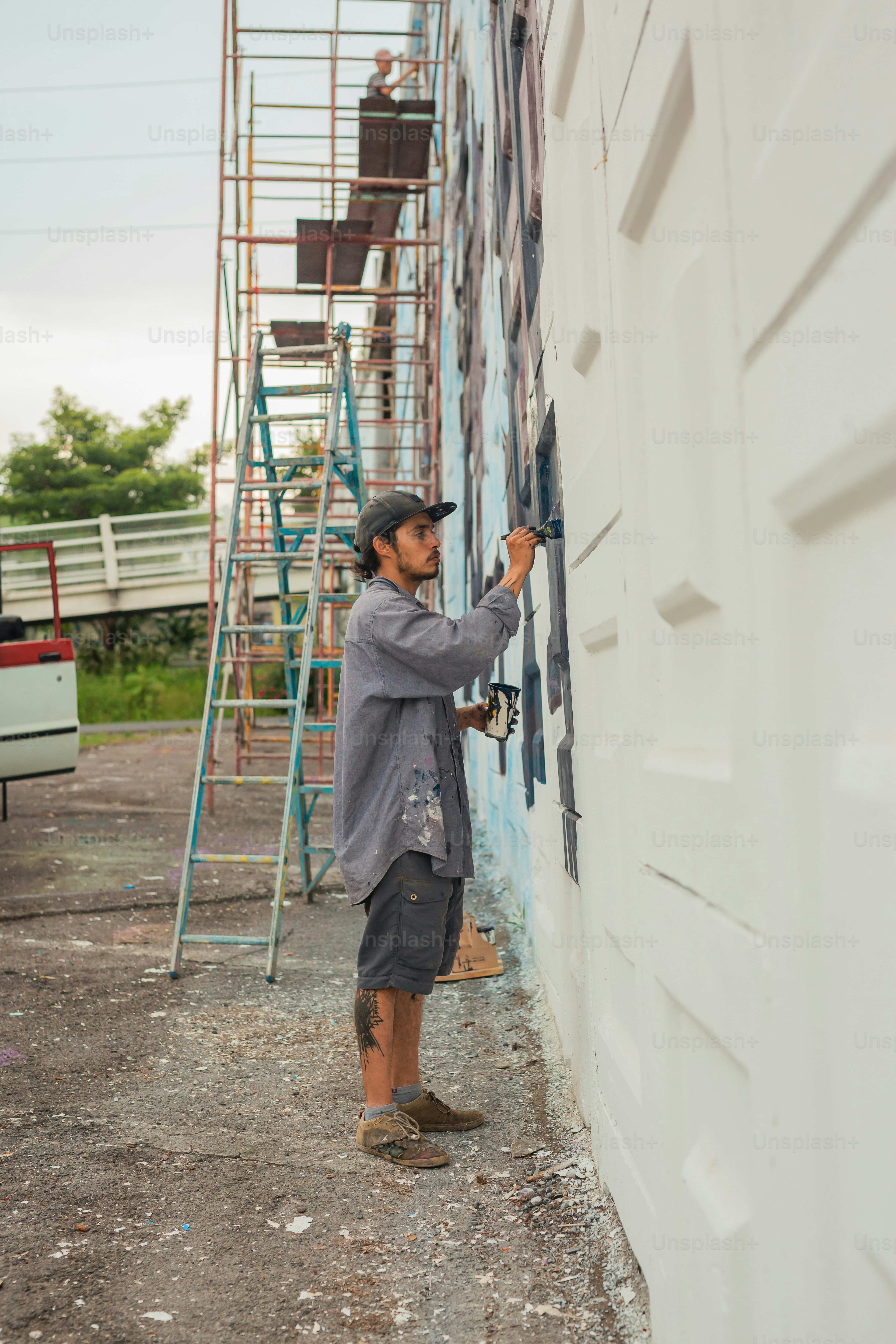 A man on a ladder painting a mural on the side of a building photo ...