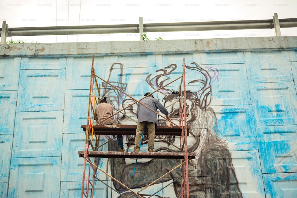two men are painting a mural on a wall