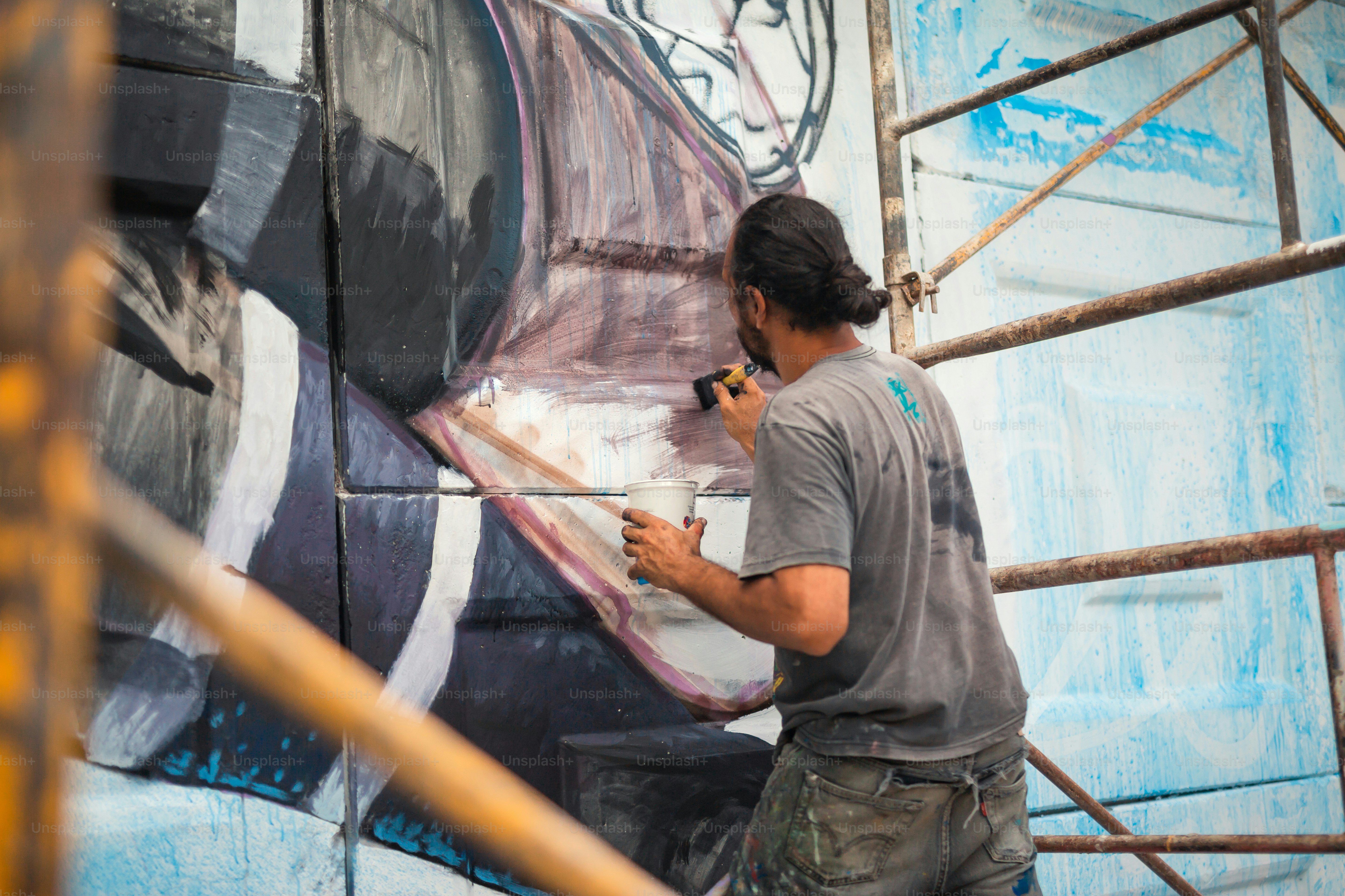 A man painting a mural on the side of a building photo – Painting Image ...