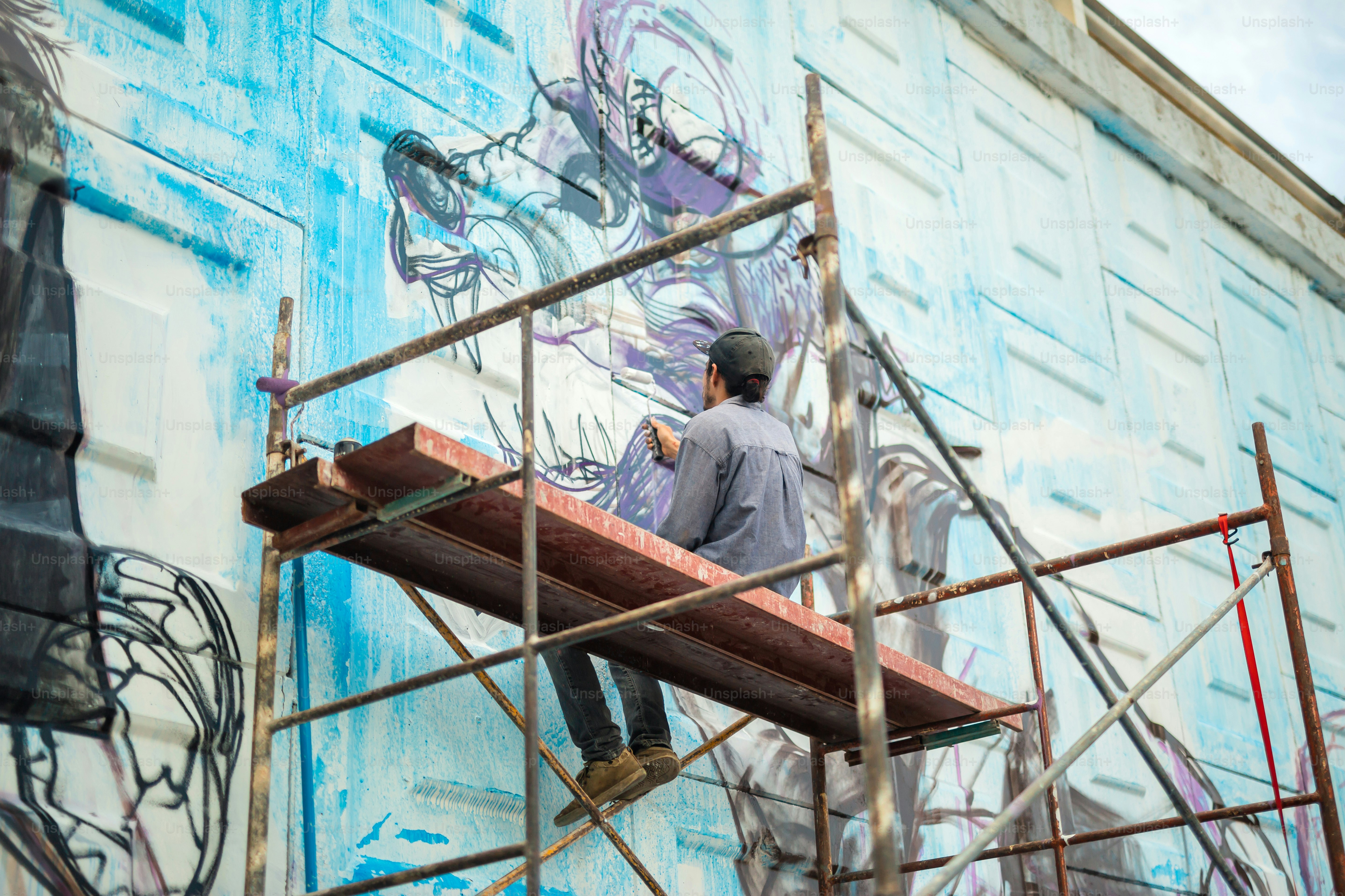 A man is painting a mural on the side of a building photo – Building ...