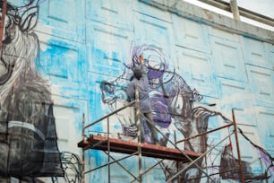um homem em um andaime pintando um mural na lateral de um prédio