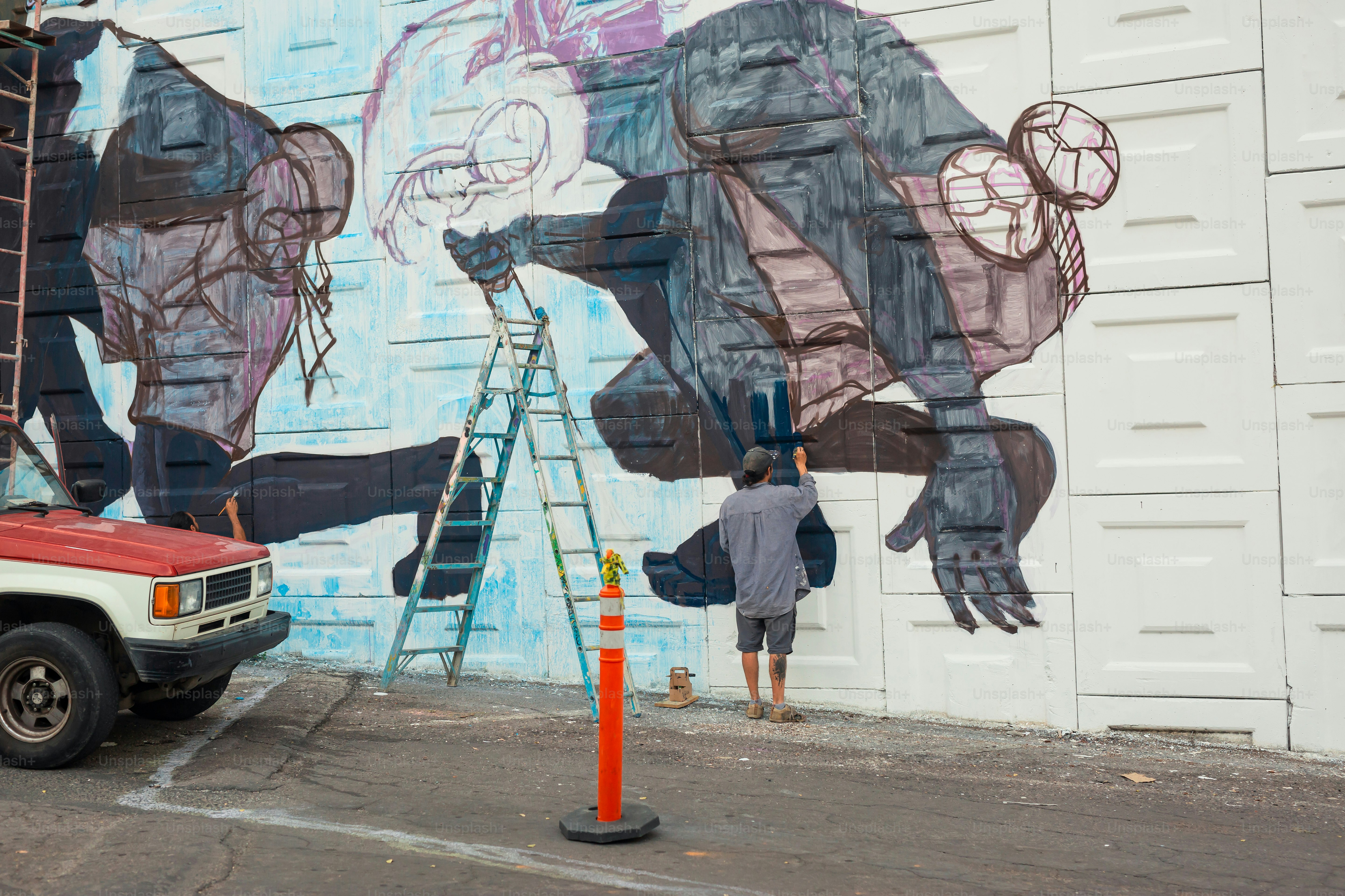 A man painting a mural on the side of a building photo – Mural Image on ...