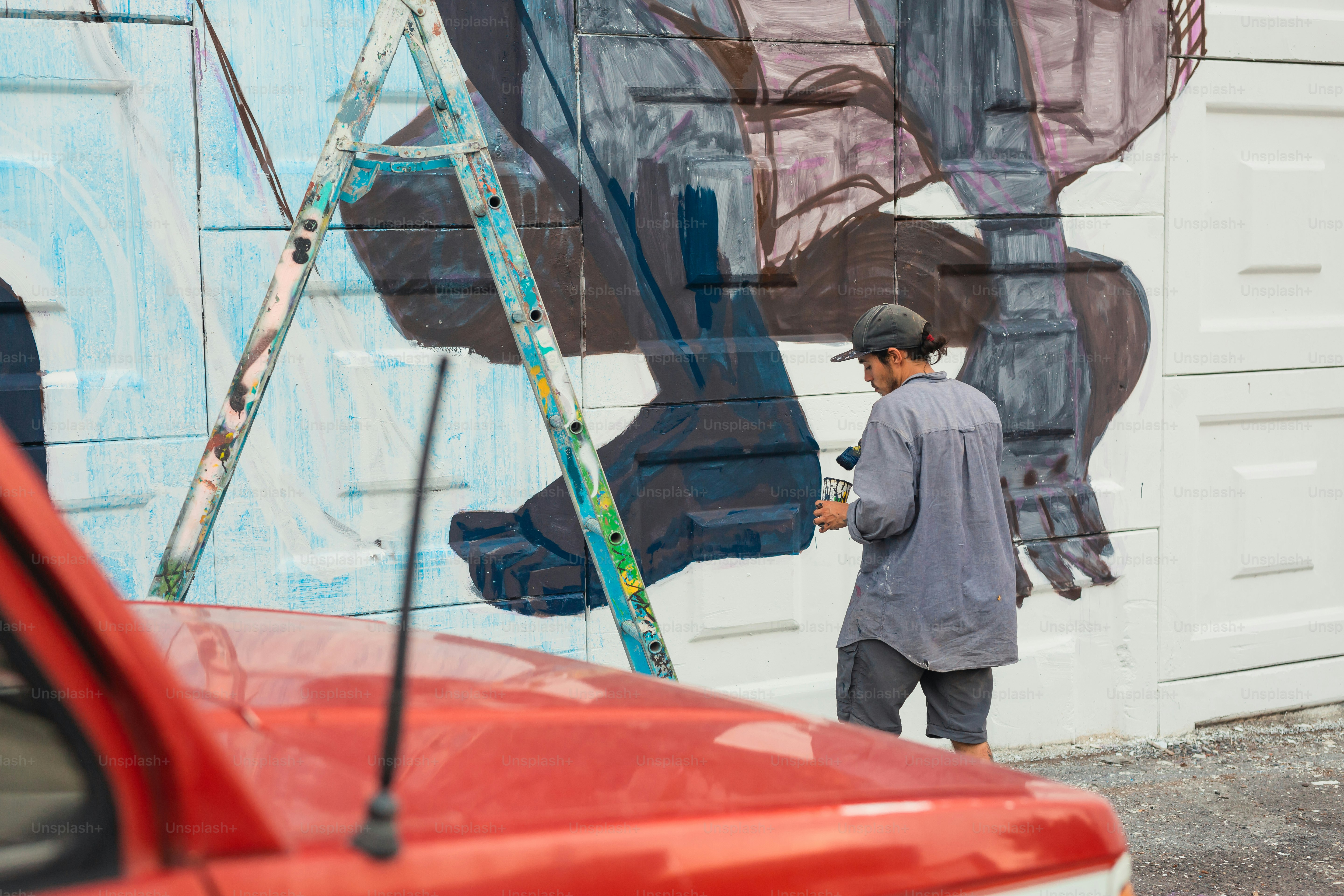 A man painting a mural on the side of a building photo – Graffiti Image ...