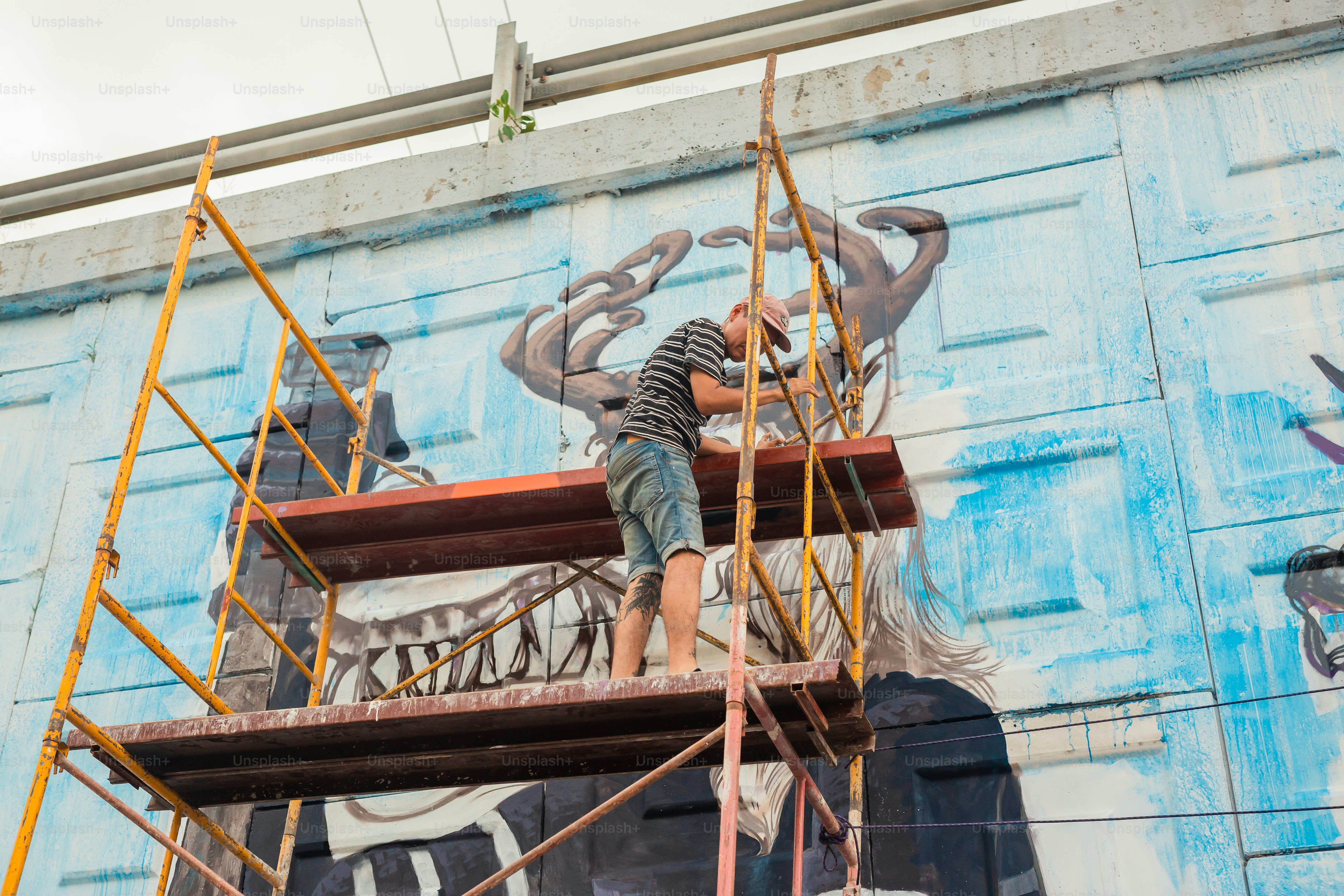 A man is painting a mural on the side of a building photo – Street art ...