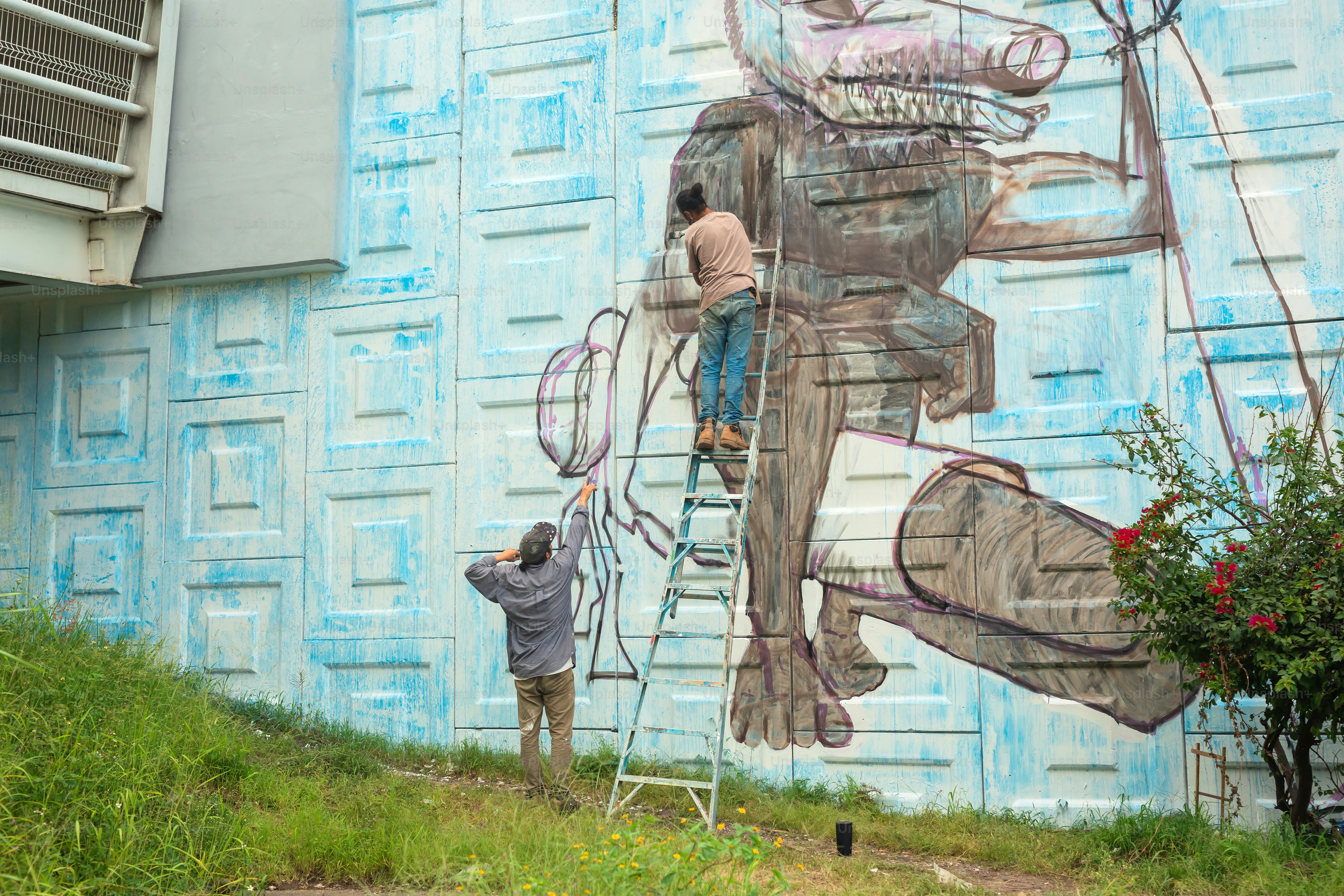 A man on a ladder painting a mural on the side of a building photo ...