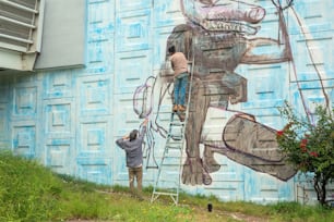 a man on a ladder painting a mural on the side of a building