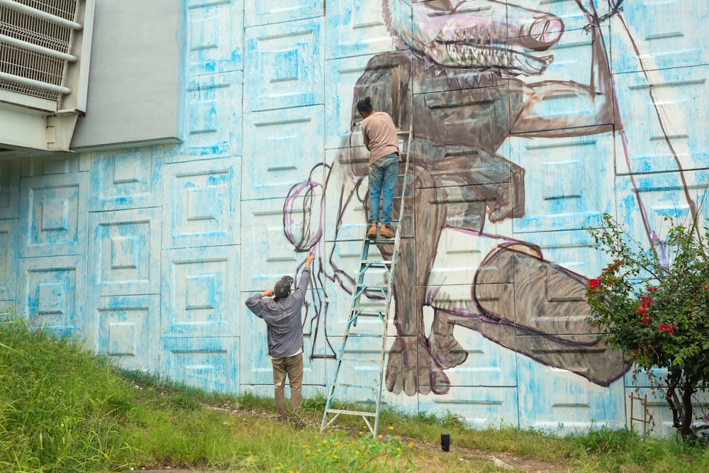 a man on a ladder painting a mural on the side of a building