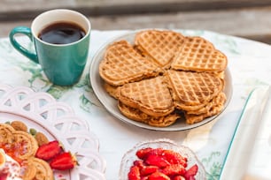 um prato de waffles e morangos ao lado de uma xícara de café